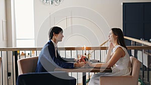 Happy couple young man and woman are talking holding hands sitting in restaurant on date together. People are wearing