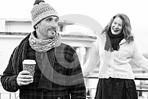 Happy couples loves drink coffee outdoor. Smiling guy holds craft cup with coffee and hiding it from girlfriend behind.