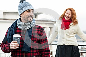 Happy couples loves coffee. Smiling guy holds craft cup with coffee hiding from girlfriend behind. Man with coffee and girlfriend