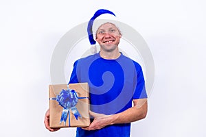 A happy courier in a blue uniform and Santa hat holds a gift box with a bow. New year and merry Christmas. The man smiles. Secure