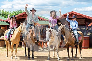 happy cowboy family of four on horsebacks waving