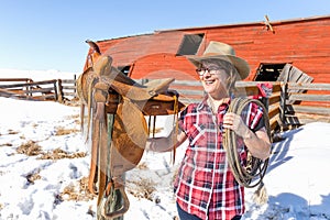 Happy cowgirl standing next to her saddle holding a rope.