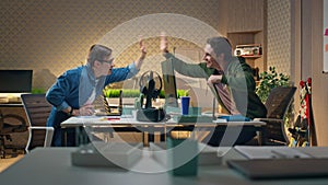 Happy coworkers giving five to each other at computer table. Guys enjoying break