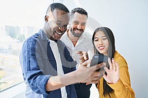 Happy coworkers looking at phone in office