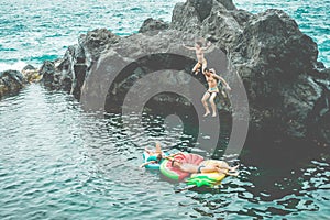 Happy crazy friends jumping inside natural sea pool with lilo - Young people having fun cliff diving inside ocean - Summer,