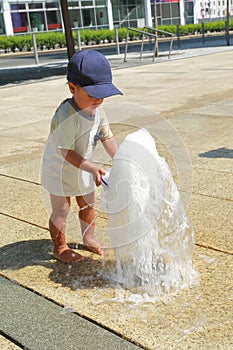 Happy curious toddler boy playing with bucket in water of fountain