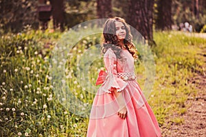 Happy curly child girl in fairytale princess pink dress dancing in summer forest