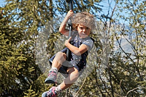 A happy curly-haired girl rides on a high swing in the mountains.