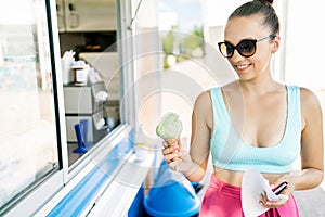 Happy customer buying ice cream from parlor, truck, van or kiosk. Takeout gelato in summer. Smiling woman holding icecream cone.