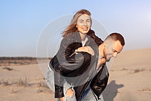 Happy and cute adorable adult couple of millennial hipsters, man with woman girlfriend on piggy back, have fun play