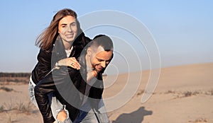 Happy and cute adorable adult couple of millennial hipsters, man with woman girlfriend on piggy back, have fun play