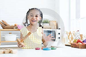 Happy cute African little child girl smiling, playing wooden blocks toy and colorful pyramid puzzle in kitchen at home, looking at