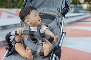 Happy and cute Asian Chinese baby boy sitting on stroller at park during evening