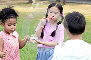 Happy cute Asian girl with curly hair African and friend blowing bubbles in green nature garden. Kids spending time outdoor