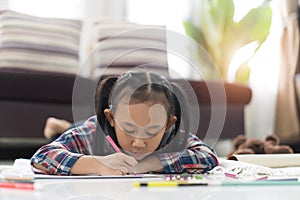 Happy cute asian little girl drawing using colorful pencils while lying on the floor