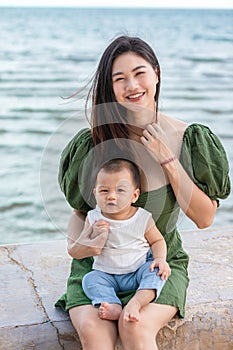 Happy cute baby boy with his mother on the beach. Summertime with baby is a quality time for Asian mommy.  Mother and baby on the