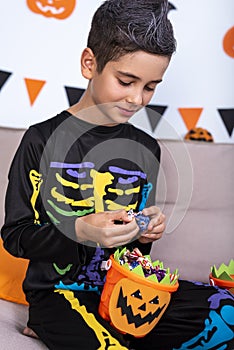 Happy cute boy in costume during Halloween party, holding pumpkin Jack-o`-lantern trying to eat candies from it