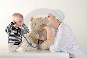 Happy cute boys playing with stethoscope in doctors office, hugging plush toy bear and smiling at camera. Female pediatrics. Copy