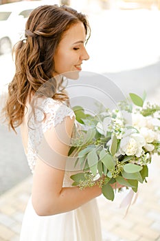 Happy cute bride keeping bouquet of flowers and wearing white dress.