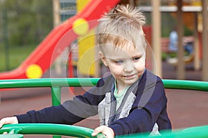 Happy cute caucasian blonde baby boy on the children playground, smiling.