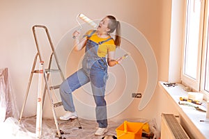 happy cute Caucasian female singing song using roller brush as a microphone. Young woman having fun during home repair