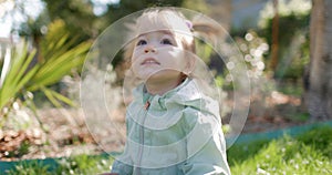 Happy cute child girl in spring garden sitting on lawn.