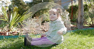 Happy cute child girl in spring garden sitting on lawn. Pretty little daughter