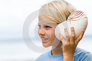 Happy cute child listening to sea in nautilus shell