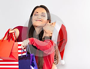 Happy cute daughter hugging and kissing with love her mother in santa clause hat and holding Christmas present packages. Portrait