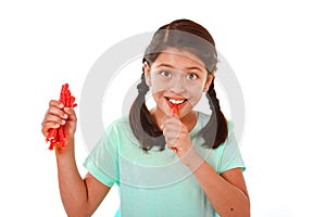 Happy cute female child licking and eating red licorice candy in kid love sweet and sugar concept