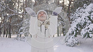 Happy cute girl, dressed in warm winter clothes, blows snow from her hands to the camera, then tosses it up. Beautiful