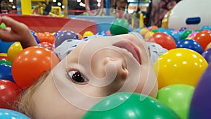 Happy cute girl having fun in ball pit in kids amusement park and indoor play center