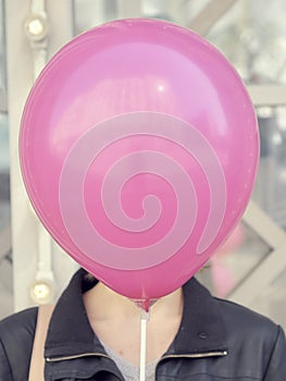 Happy cute girl hiding her face behind pink balloon