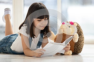 Happy cute girl lying on heating floor reading book.