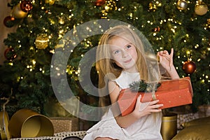 Happy cute girl sit near christmas tree with red gift box.