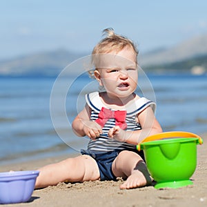 Happy cute girl in swimsuit playing with sand on beach