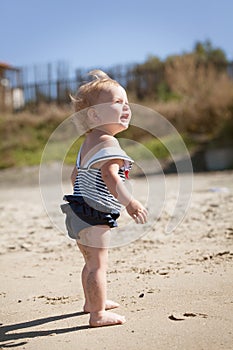 Happy cute girl in swimsuit playing with sand on beach
