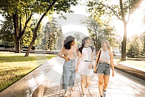 Happy cute girls of different races are chatting and walking in the park. Charming friends laugh and have fun together on the photo