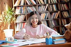 Happy cute hispanic indian school girl studying at table at home, portrait.