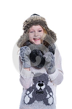 Happy cute kid posing in the studio. Wearing winter clothes. Knitted woolen sweater and mittens. Ear flaps fur cap.