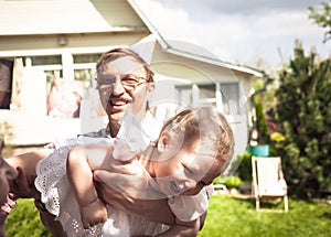 Happy cute laughing baby girl having fun with active senior grandfather outdoors on backyard