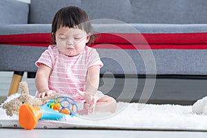 Happy cute little 7 months old multiracial, asian and caucasian, newborn baby girl sitting on floor in living room at home.