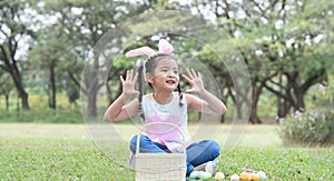 Happy cute little Asian child girl hunting Easter eggs, wearing bunny ears. kid counting eggs in basket after play hunt eggs game