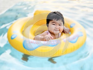 Happy cute little baby child learning to swim with swimming ring in an indoor pool. Smiling little child, newborn girl having fun