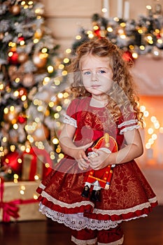 Happy cute little blonde girl with long hair in a red dress, waiting for Christmas and New year opens a gift on the