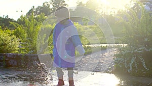 Happy cute little boy chid running playing having fun jumping through puddles in raincoat and rubber boots. laughing and