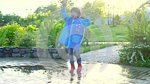 Happy cute little boy chid running playing having fun jumping through puddles in raincoat and rubber boots. laughing and