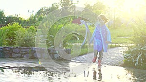 Happy cute little boy chid running playing having fun jumping through puddles in raincoat and rubber boots. laughing and