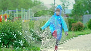 Happy cute little boy chid running playing having fun jumping through puddles in raincoat and rubber boots. laughing and