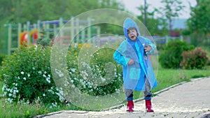 Happy cute little boy chid running playing having fun jumping through puddles in raincoat and rubber boots. laughing and